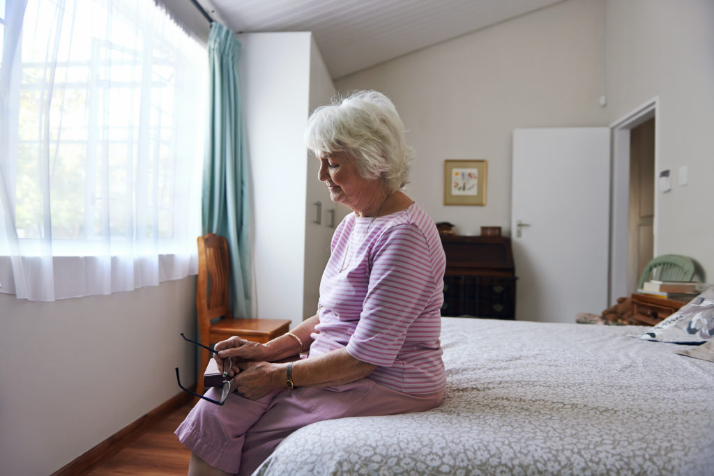 elderly woman sitting at the edge of her bed alone