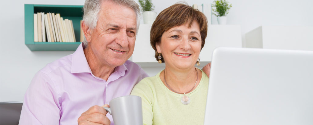 elder couple happily looking at a computer together